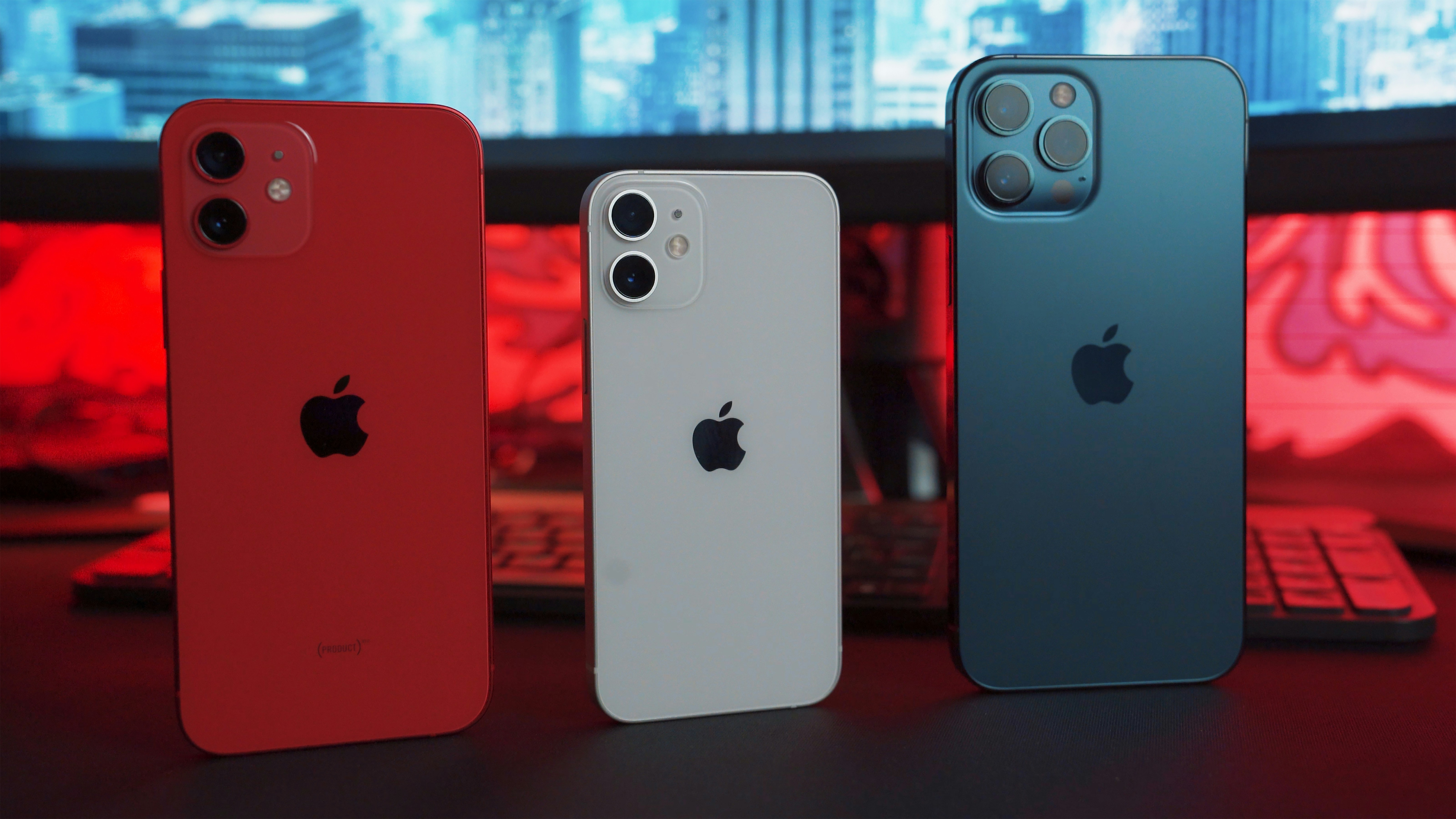 Three iPhones in red, gray, and blue standing together